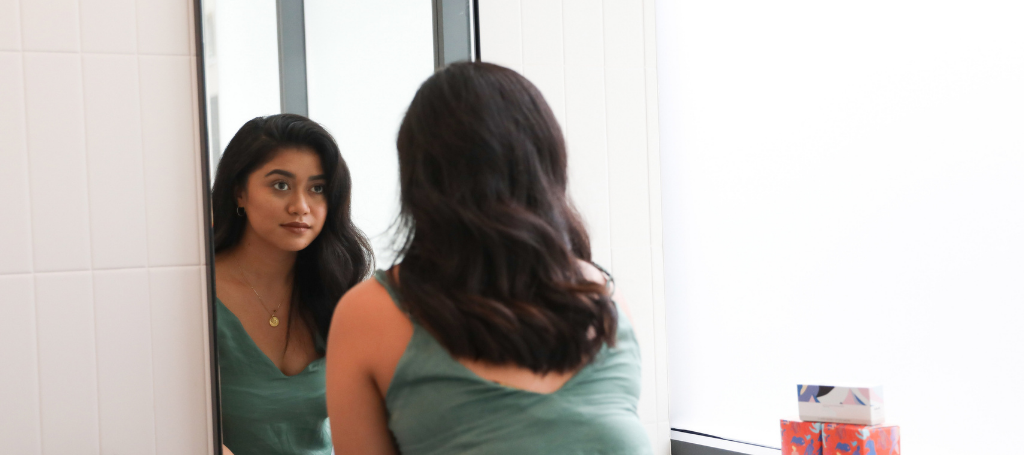 a woman looks at her reflection in a bathroom mirror