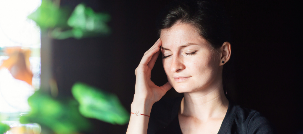 What Is Migraine Threshold Theory? a woman with her eyes closed holds her hand to her forehead because of a migraine